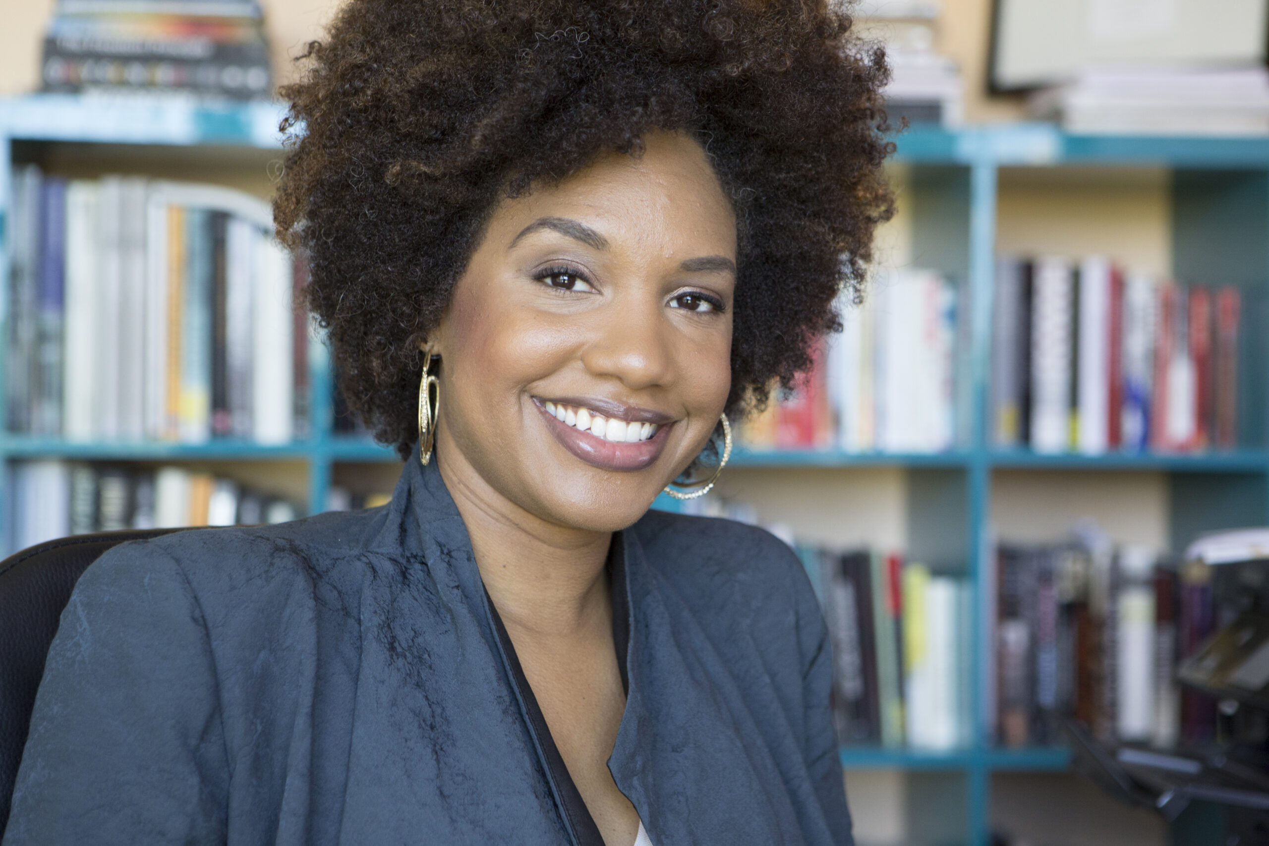 Headshot of photographer LaToya Ruby Frazier in navy top with blurred bookshelves in the background